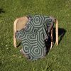 The woven blanket draped over a chair placed on grass, showcasing its geometric design.