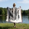 Woman standing with her back to the camera, covering herself with the modern monochrome blanket on grass near a lake.