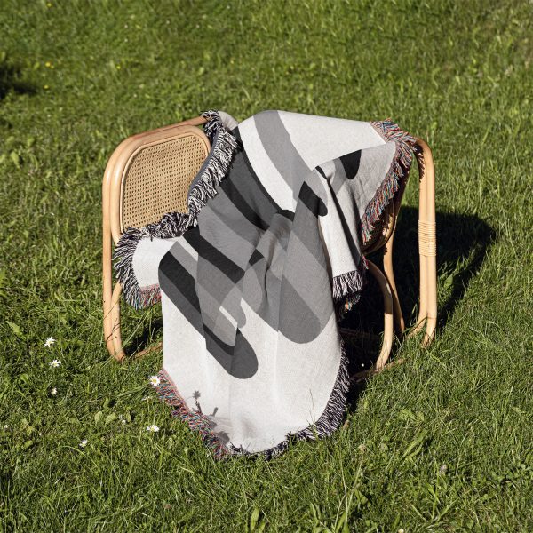 Woven blanket draped over a chair on grass, showcasing an abstract monochrome pattern.