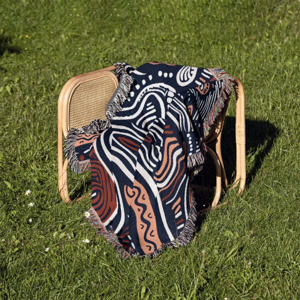 An organic-patterned woven blanket placed on a chair outdoors on vibrant green grass.