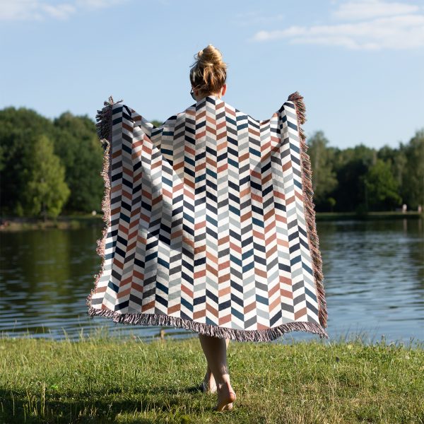 Back view of a person by a lake, wrapped in the Scandinavian Chevron Harmony Woven Blanket.