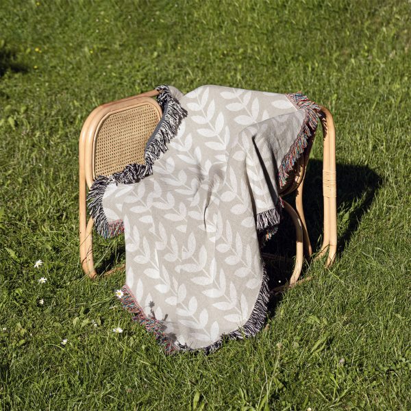 Scandinavian Minimalist Leaf Woven Blanket placed on a chair outdoors on a grassy lawn.