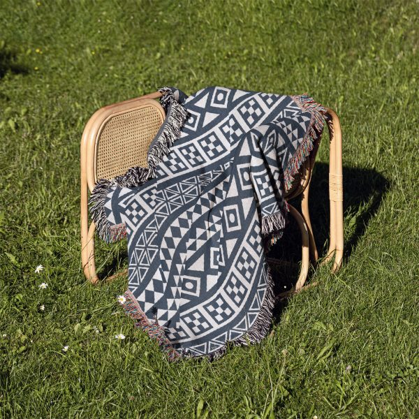 Scandinavian Tribal Stripe Woven Blanket placed on a chair outdoors on a grassy lawn.