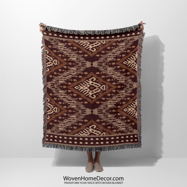 A person holds a tribal-patterned woven blanket in rich brown and beige tones