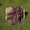 A tribal-patterned woven blanket laid over a chair outdoors on lush green grass.