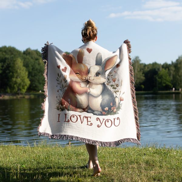 A person standing on grass by a lake, draped in the Adorable Bunny Love blanket, view from behind