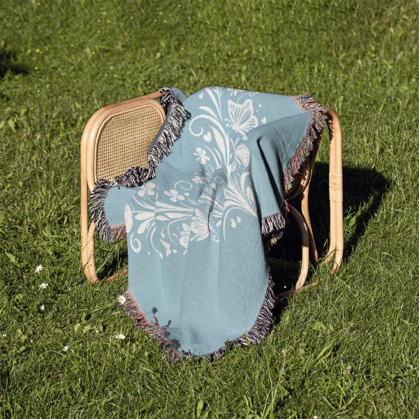 The woven blanket featuring butterfly and heart designs folded on a chair placed on grass.