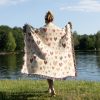 A woman by the lake, wrapped in the Enchanted Hearts Woven Blanket, viewed from behind.