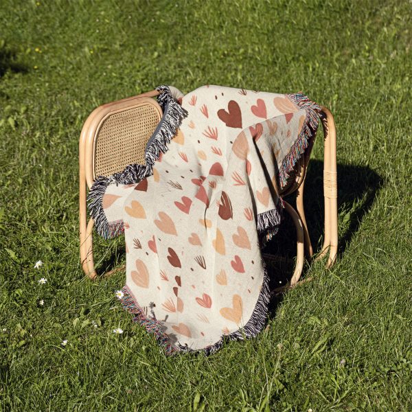 The Enchanted Hearts Woven Blanket placed on a chair outdoors, surrounded by green grass, evoking a peaceful mood.