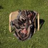 The woven blanket with a skeleton couple design folded on a chair placed on grass.