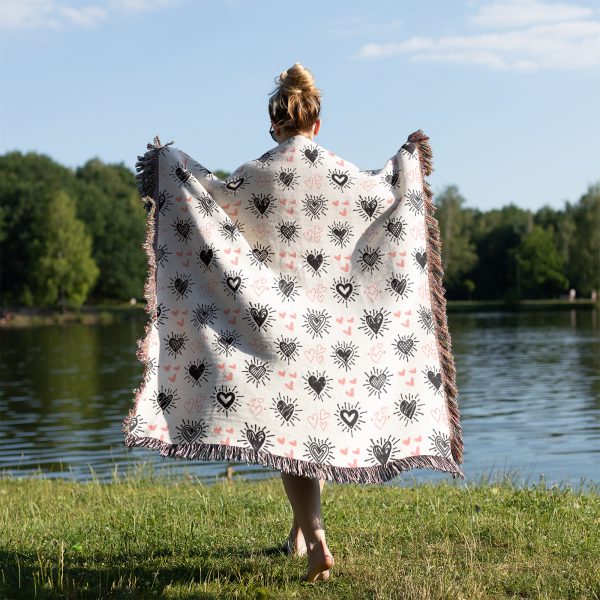 A woman by a serene lakeside, wrapped in the Floral Burst Woven Blanket, with her back turned.