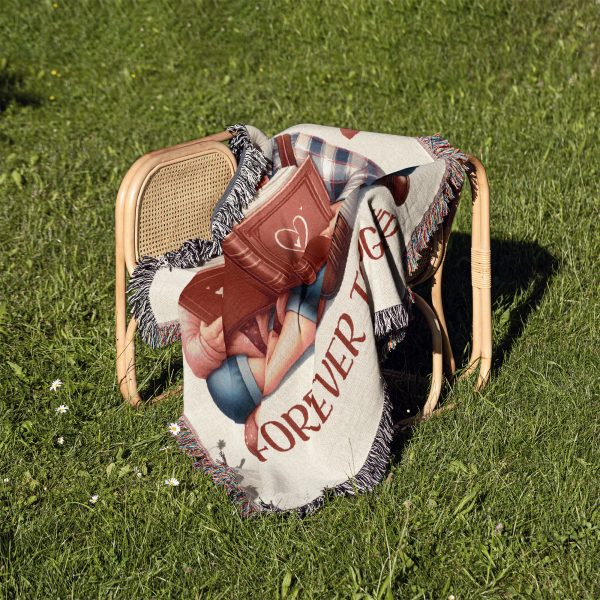 The woven blanket with an elderly couple illustration folded on a chair placed on grass.