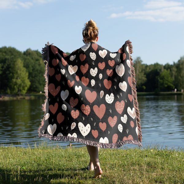 A woman stands by a lakeside, draped in the Heart Pattern Woven Blanket, with her back to the camera.