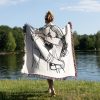 A person standing by a lake, wrapped in the Minimalist Love Embrace woven blanket, view from behind.