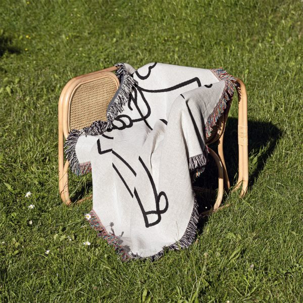 The Minimalist Love Sketch blanket folded and placed on a chair outdoors on the grass