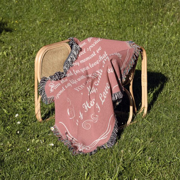 The Romantic Girlfriend Woven Blanket folded on a chair placed on a grassy area.