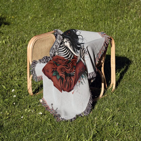 The Romantic Skeleton Couple blanket folded and placed on a chair outdoors on a grassy background