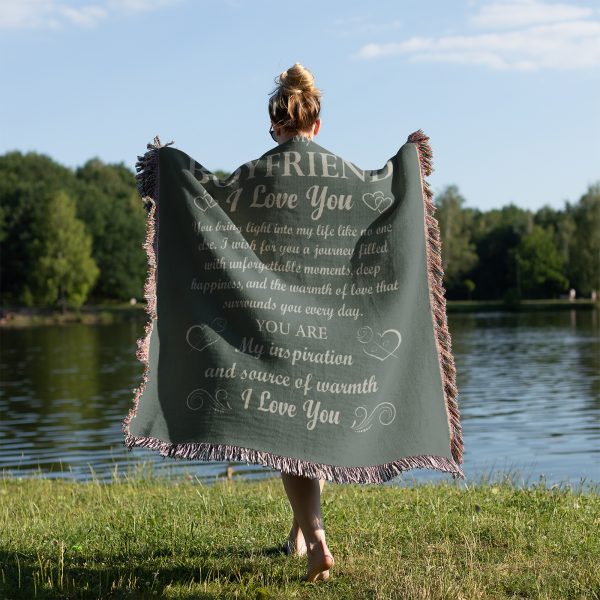 A woman by a tranquil lake, wrapped in the To My Boyfriend Woven Blanket, with her back to the camera.