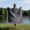 A woman stands at the lakeside, wrapped in the To My Husband Woven Blanket, with her back facing the camera.