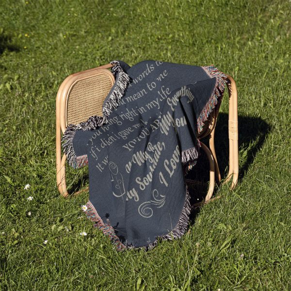 The To My Husband Woven Blanket folded on a chair outdoors, placed on a green lawn.