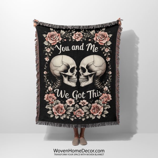 A woven blanket featuring skeleton skulls and roses, held up by a person.