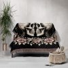 The woven blanket with skeleton skulls and roses draped over a sofa.